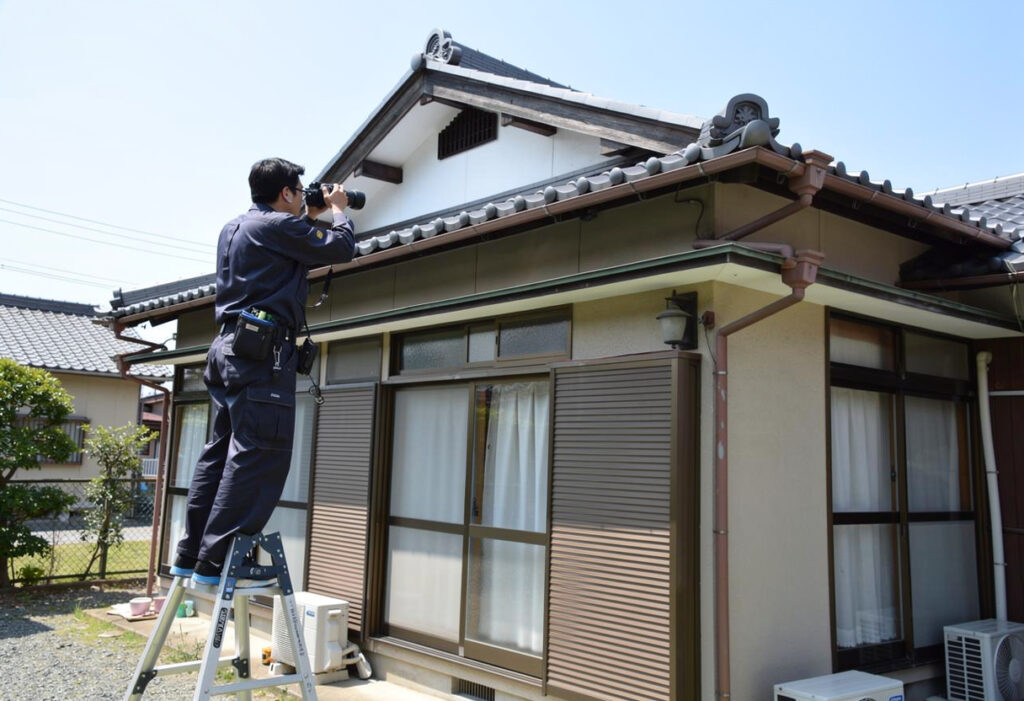専門業者が屋根に上らず地上から双眼鏡とカメラで棟板金の被害状況を確認している様子
