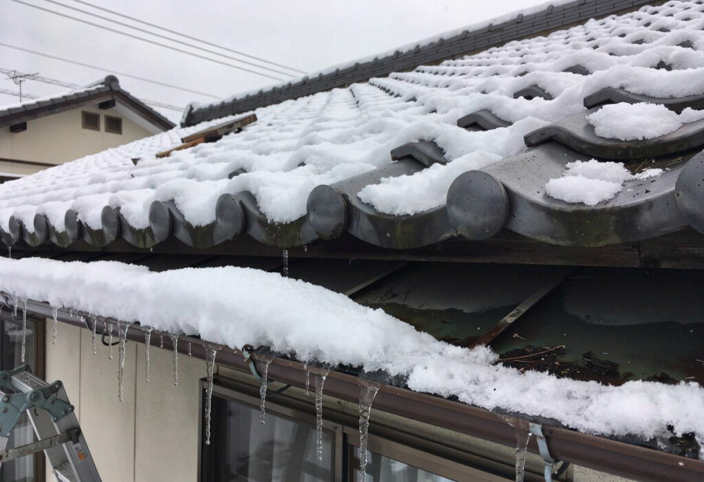 大雪の重みで屋根瓦がずれ、雨樋が歪んで垂れ下がっている住宅の被害状況