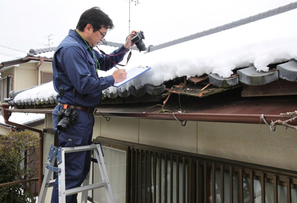 専門業者が雪害を受けた屋根や雨樋を調査し、写真で記録している様子