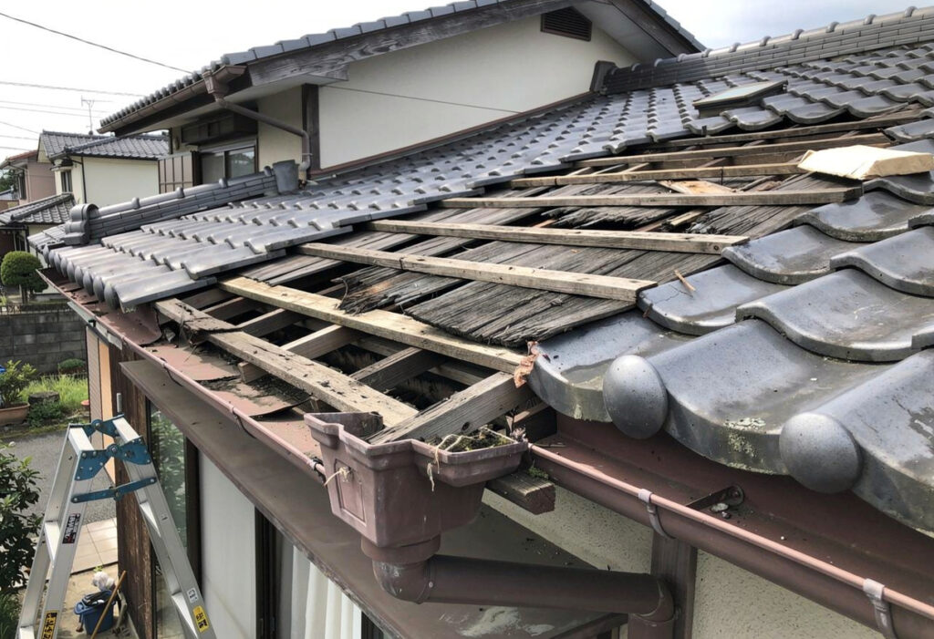 台風の後に屋根の瓦がずれて一部がめくれている様子や雨樋が外れかけている状態を示す写真