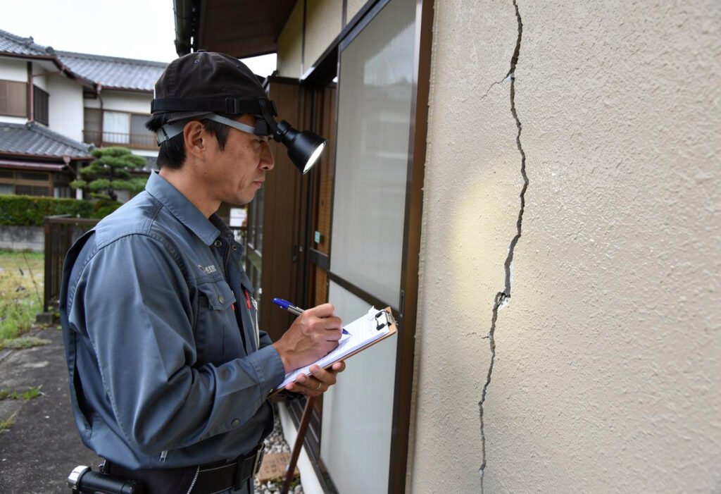 調査員が住宅の外壁のひび割れを確認しながら記録を取っている現地調査の様子
