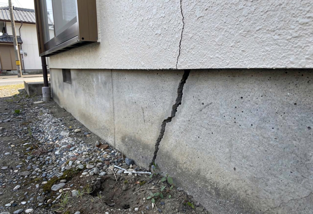住宅の基礎に入った斜めのひび割れと外壁のクラックを確認している様子